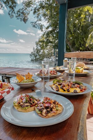 A table with various dishes and drinks, overlooking a body of water. - Blue b7 departamentos (Bacalar)