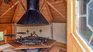 Een rustieke houten hut met een centraal geplaatste houtkachel, banken en een raam.