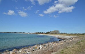 A coastal landscape with a rocky shoreline, calm water, and a clear sky.