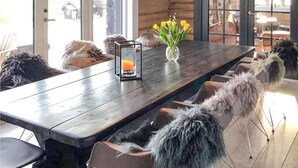 A wooden dining table with a candle, a vase with yellow flowers, and fluffy chairs.
