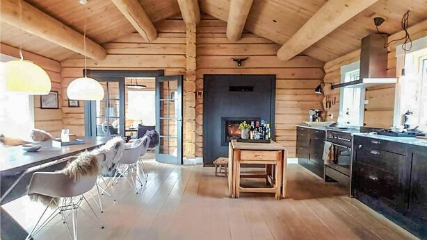 A log cabin interior with a dining area, kitchen, and fireplace.