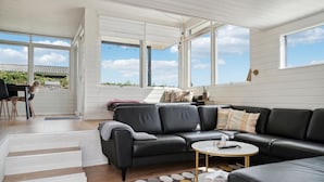 A spacious living room with a black leather sofa, a round coffee table, and a view of the outdoors through large windows. - 3 bedroom nice home in Rønde (Rønde)