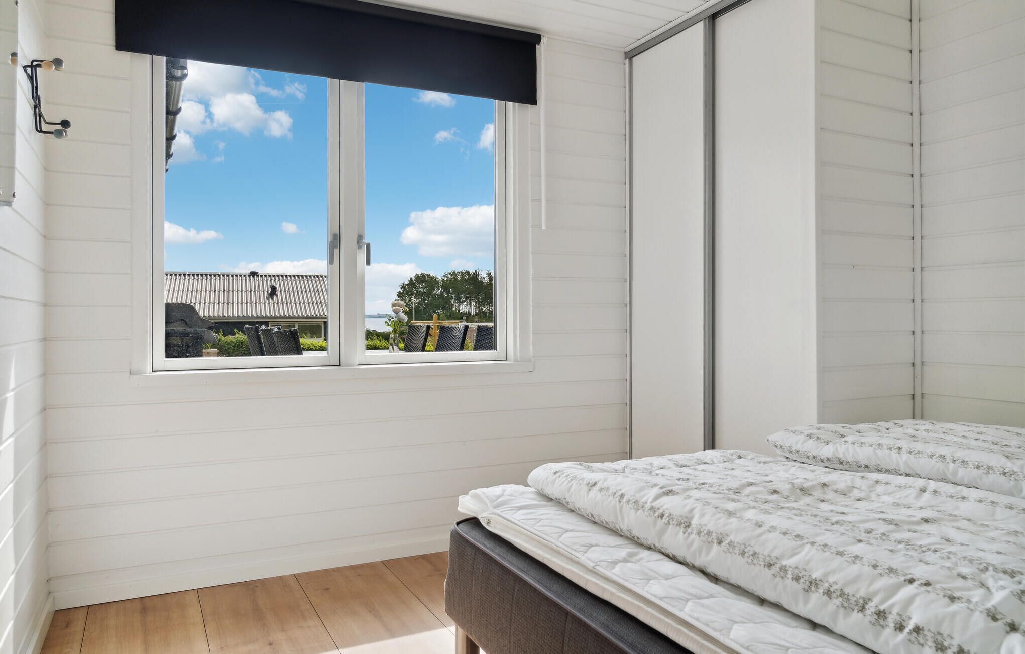 A bedroom with a bed, a window with a view of the outside, and a wooden floor.