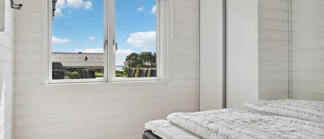 A bedroom with a bed, a window with a view of the outside, and a wooden floor.