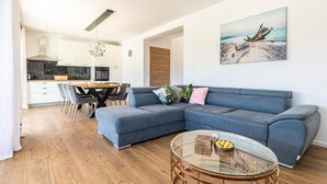 A modern living room with a blue sofa, a glass coffee table, and a painting of a beach scene. - Stunning home in Kastel Novi (Kastel Novi)