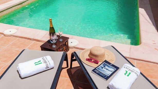 A poolside setting with a lounge chair, a bottle of champagne, a glass, a straw hat, and a book titled "Rural Days". - Alojamiento rural Aloe Pozo Alcón by Ruralidays (Jaén)