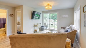 Un salon avec un canapé beige, une petite table d’appoint et un téléviseur fixé au mur.