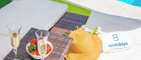 A table with a glass of white wine, a bowl of strawberries, and a straw hat with a towel.