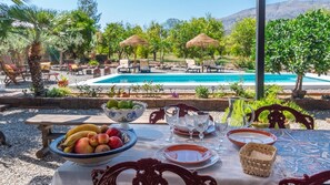 Mesa de comedor al aire libre con vista a la piscina, rodeada de sillones de descanso y sombrillas.