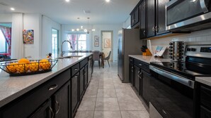 A modern kitchen with dark cabinetry, stainless steel appliances, and a central island with a fruit bowl. - Family Ready Pool Villa with Star Wars Game Room, Karaoke (Kissimmee)