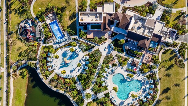 An aerial view of a resort with multiple swimming pools, a large central pool, and a variety of outdoor seating areas surrounded by palm trees and greenery. - Family Ready Pool Villa with Star Wars Game Room, Karaoke (Kissimmee)