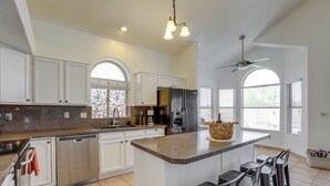 A spacious kitchen with white cabinets, a granite countertop, and a central island with bar stools. - Cookout Ready! Desert Oasis w/ Pool in Goodyear (Goodyear)