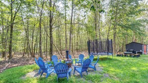 An outdoor seating area with blue chairs and a table, surrounded by trees. - 'A Time to Remember' Home in Tobyhanna w/ hot tub (Tobyhanna)