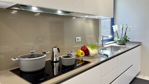 Eine moderne Küche mit Einbauherd, Wasserkocher und Topf auf einer Induktionskochplatte. Ein Spülbecken mit Armatur und ein Fenster darüber.