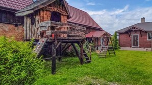 A rustic wooden building with a red-tiled roof, a wooden swing set, and a wooden water wheel. - 2 bedroom gorgeous home in Darlowo (Darlowo)