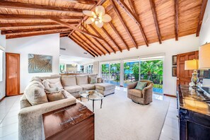 Uma sala de estar ampla com teto alto, grandes janelas e vista para o verde lá fora.