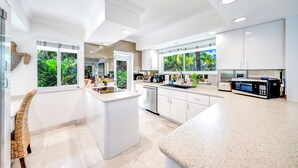 Una cucina moderna con mobili bianchi, un'isola centrale e ampie finestre con vista sulle zone tropicali.