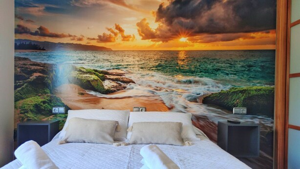 A bedroom with a bed, pillows, a nightstand, and a wall mural of a sunset over the ocean. - Desconectaengalicia Townhouse Vichona 2.5 km from the center of Sanxenxo (Forxán)