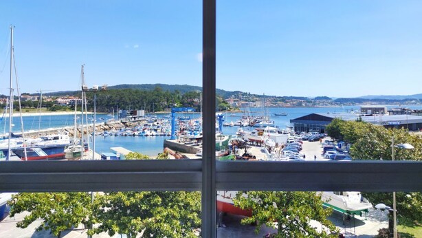 Un puerto deportivo con barcos amarrados, cielo despejado y una vista distante de colinas.