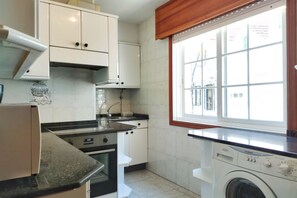 A kitchen with white cabinets, a built-in oven, a washing machine, and a window with a view of buildings.