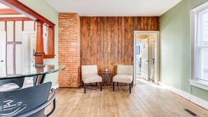 A room with a wooden floor, two chairs, a glass table, and a brick wall. - Pet-Friendly Penn Yan Home: Wineries, Parks, Lakes (Penn Yan)