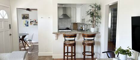 A modern kitchen with a central island, wooden chairs, and a ceiling fan.