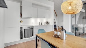 Eine moderne Küche mit weißen Schränken, einem eingebauten Backofen und einer Essecke mit Holztisch und Stühlen.