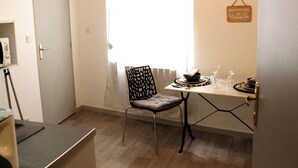 A small, well-lit room with a dining table set for two, a chair, and a window with curtains. - THE ISLE PARADISE (Saint-Quentin)