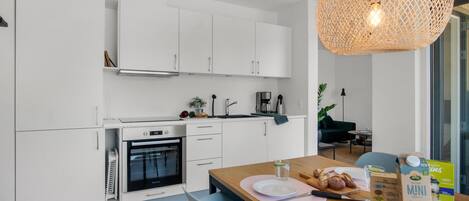 A modern kitchen with white cabinets, a built-in oven, and a dining area with a wooden table.