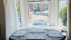 Una habitación con ventanal, una mesa con individuales, dos sillas rojas y un radiador.