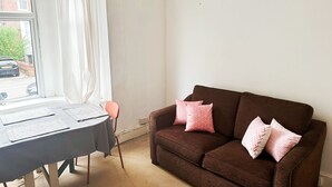 Una habitación con un sofá marrón, una mesa con una silla y una ventana con cortinas.
