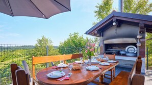 An outdoor dining area with a wooden table set for four, a grill, and a view of the countryside. - 2 bedroom lovely home in Kladje (Kladje)