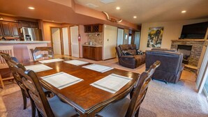 A spacious living room with a large wooden dining table surrounded by chairs, a fireplace, and a stone fireplace.