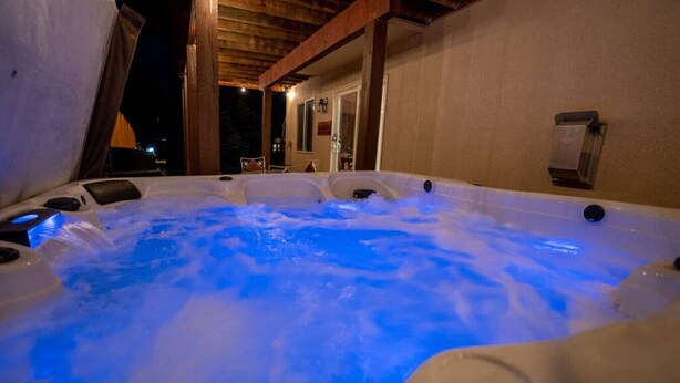 A hot tub with blue lighting, wooden beams, and a view of the outside at night.