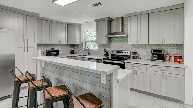 A modern kitchen with white cabinets, a large island with bar stools, a built-in oven, and a microwave. - Updated 4 bedroom home in Oragnefield (Orange)