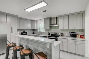 A modern kitchen with white cabinets, a large island with bar stools, a built-in oven, and a microwave.