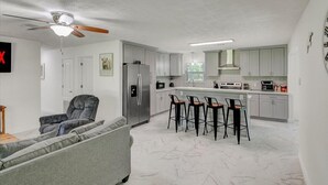 A modern kitchen with white cabinets, a refrigerator, a stove, and a bar area with stools. - Updated 4 bedroom home in Oragnefield (Orange)
