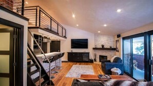 Una sala de estar moderna con una escalera, un televisor de pantalla plana, una chimenea y un ventanal grande.