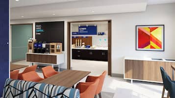 A modern dining area with a wooden table and orange chairs, a coffee station with branded coffee makers, and a kitchen area with a sign for breakfast.
