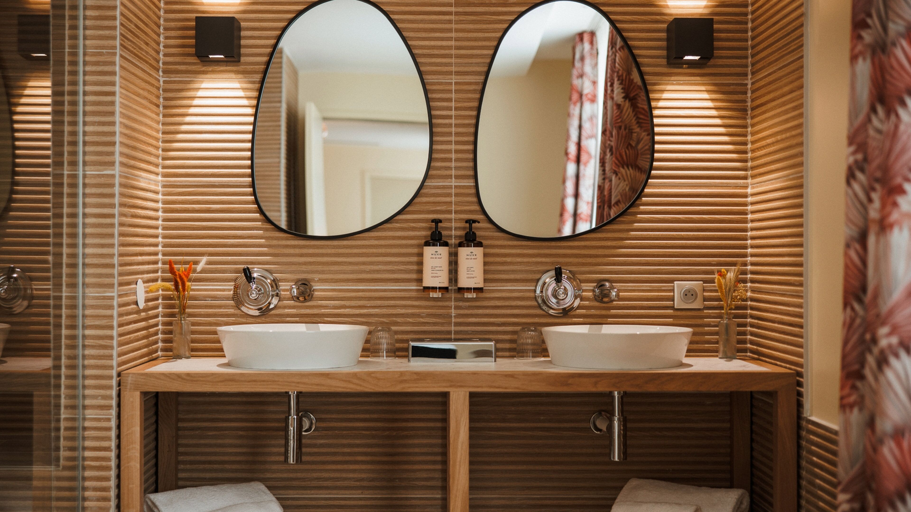 A modern bathroom with two sinks, wooden paneling, and two large mirrors.