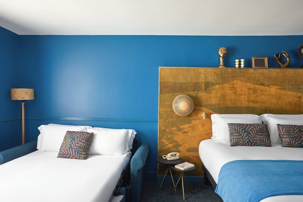Ein Hotelzimmer mit zwei Betten, einer blauen Wand und einem hölzernen Kopfteil.