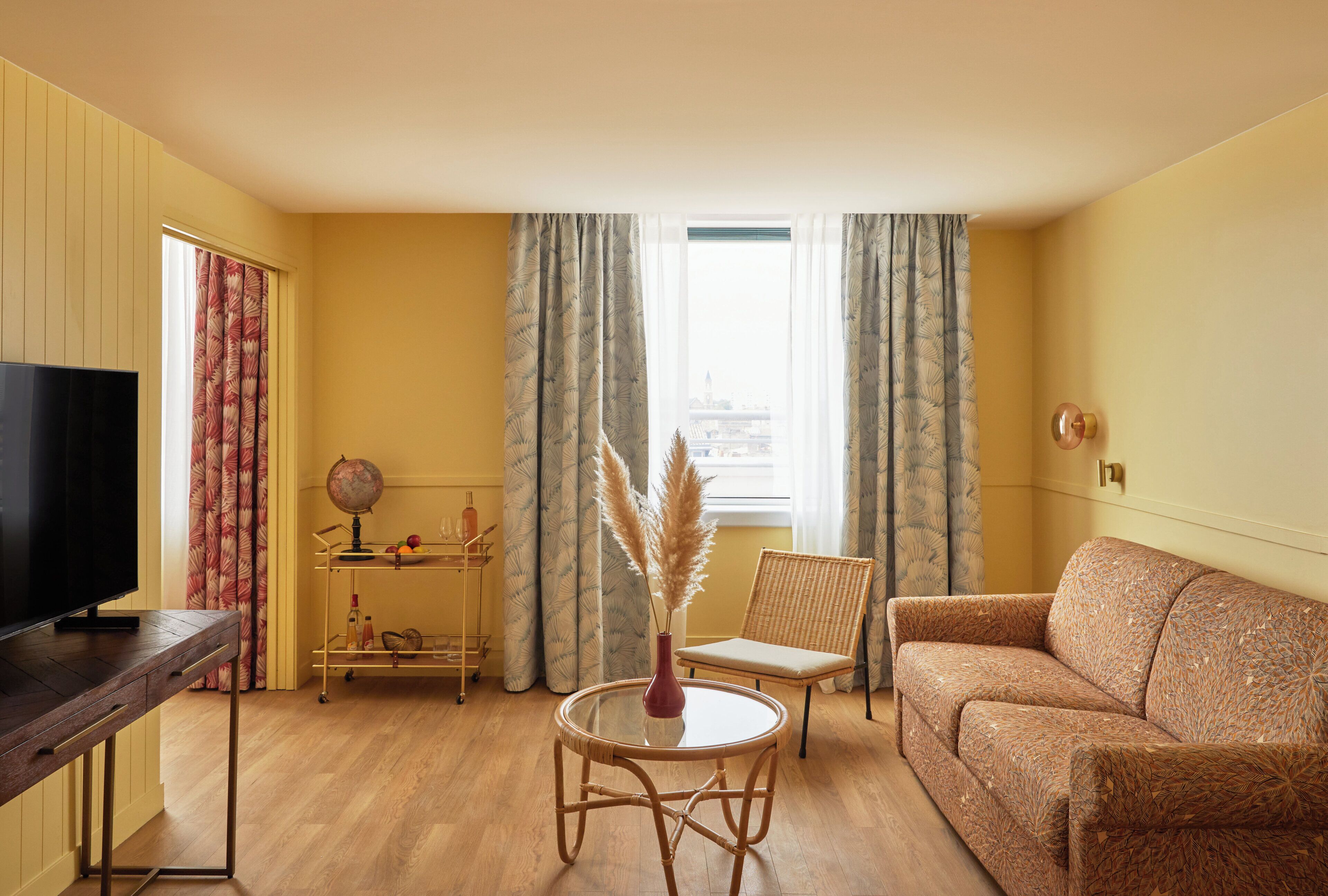 A living room with a television, a round table with a vase, a wicker chair, and a sofa.