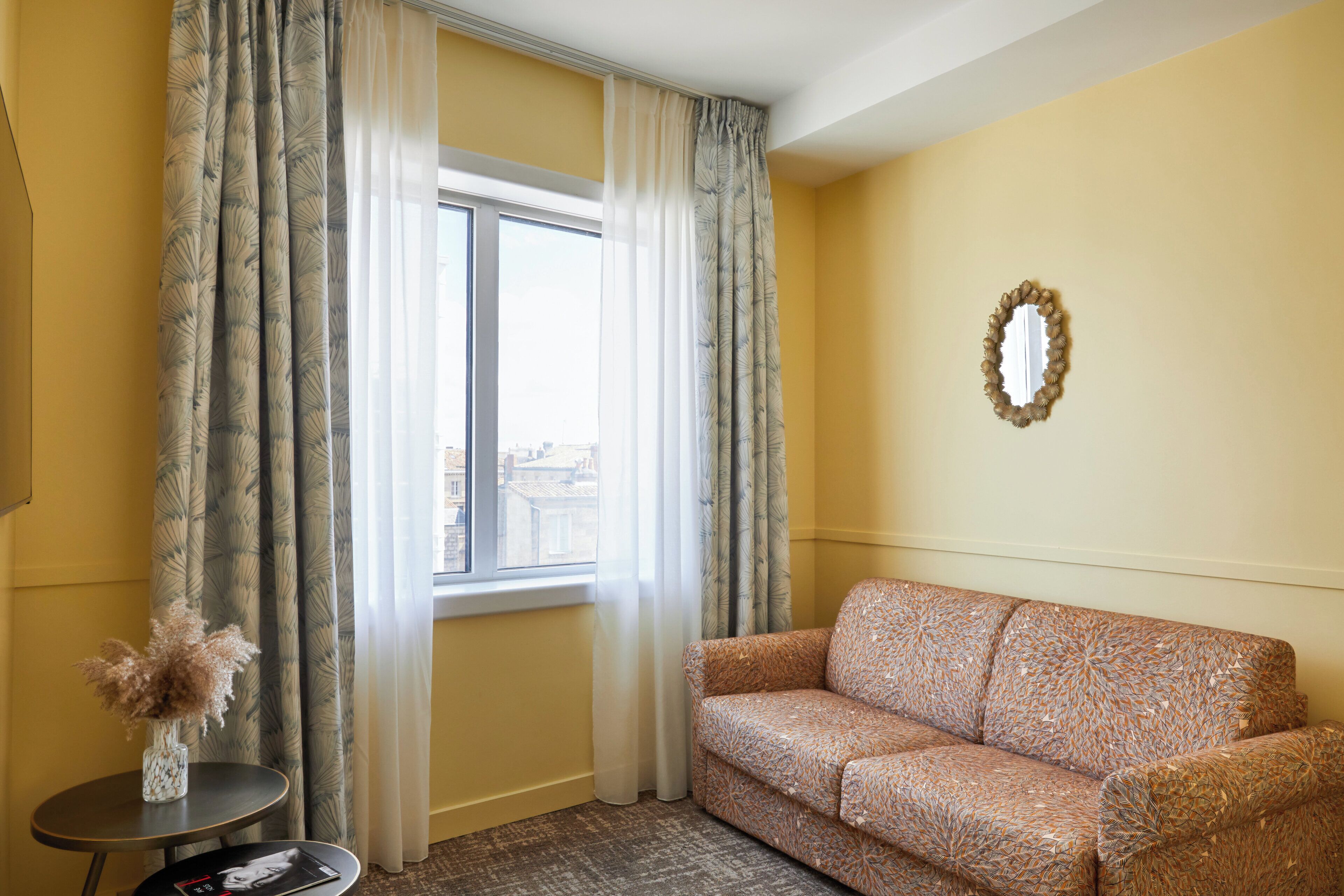 A room with a sofa, a small table with a vase, and a window with curtains.