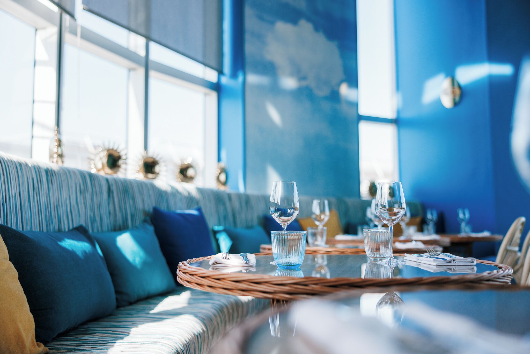 A dining area with a table set for two, featuring a woven placemat, a glass of water, and a wine glass.