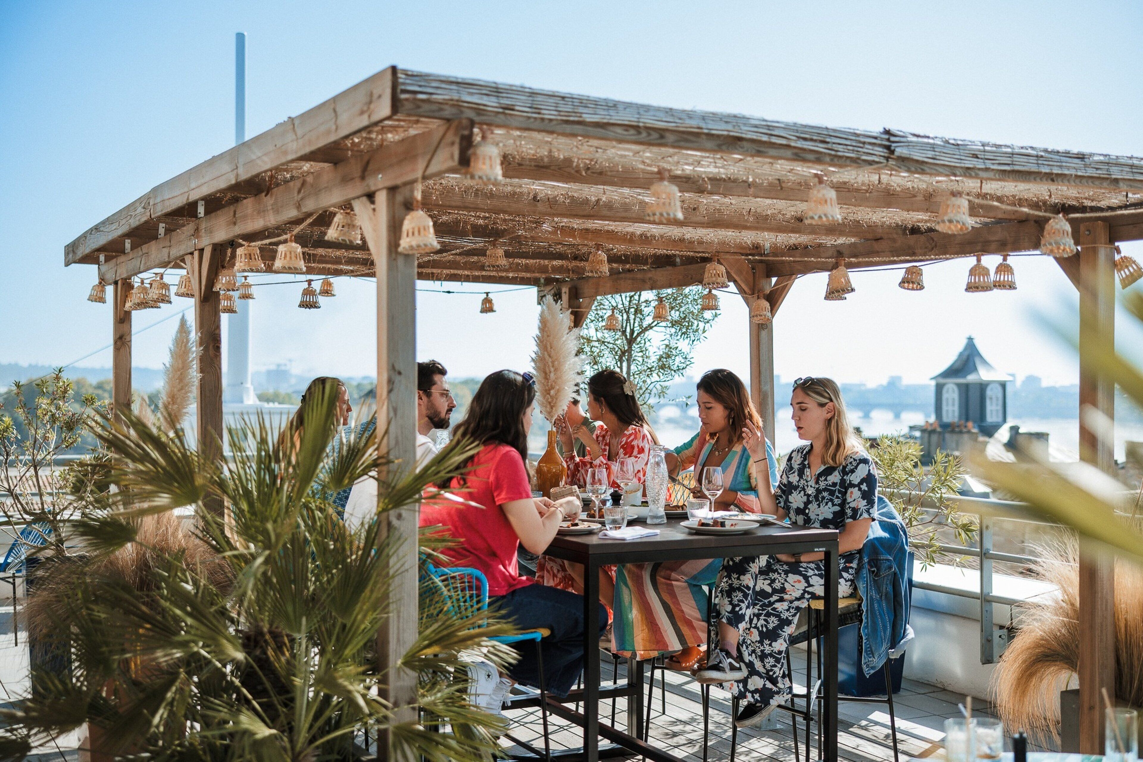 A group of people dining at an outdoor table with a wooden pergola overhead.