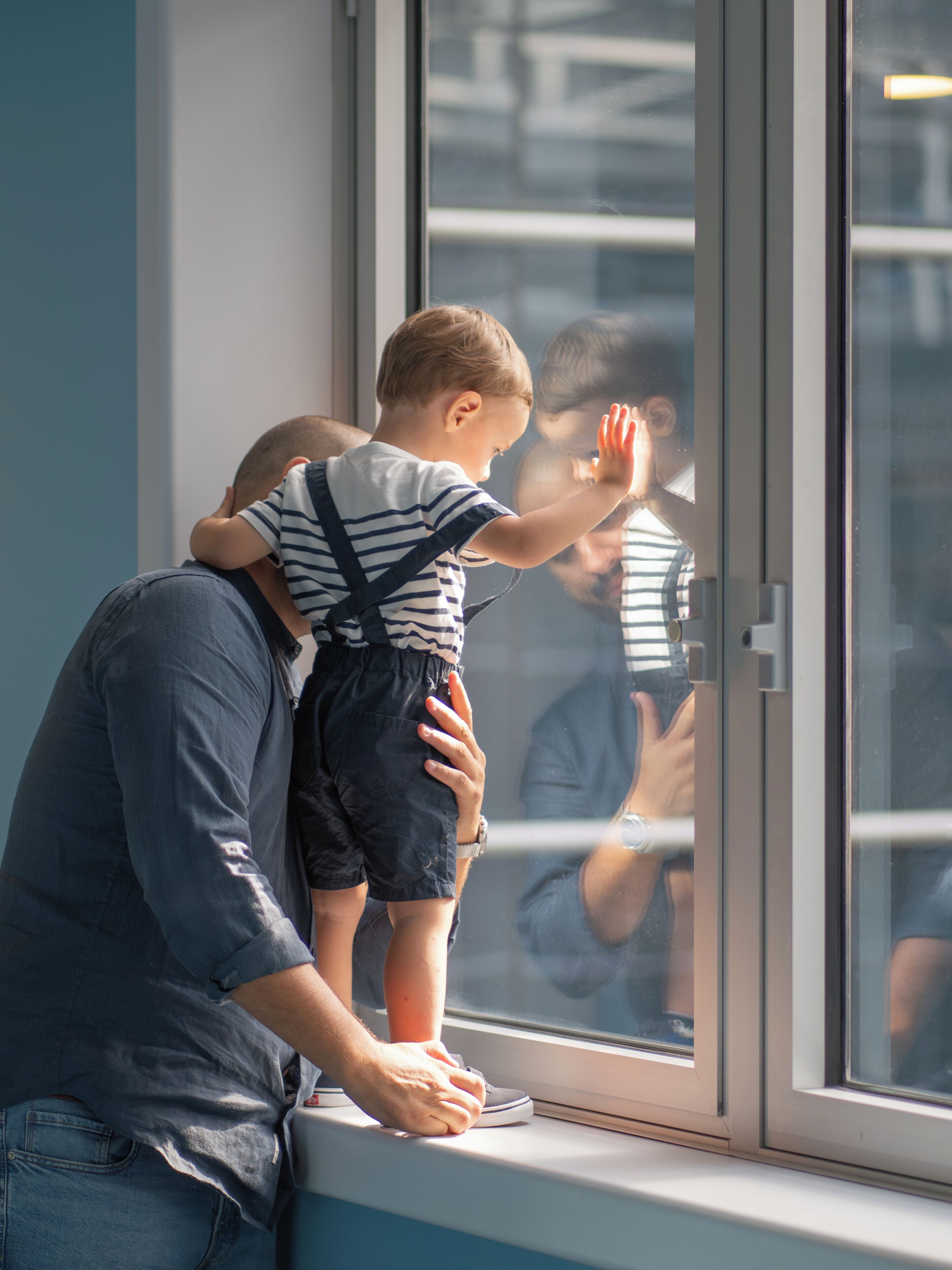 A person holding a child by the window, with a reflection visible.