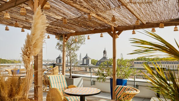 A rooftop terrace with wicker furniture, a thatched roof, and a view of city buildings. - Hotel Indigo Bordeaux Centre Chartrons by IHG (Bordeaux)