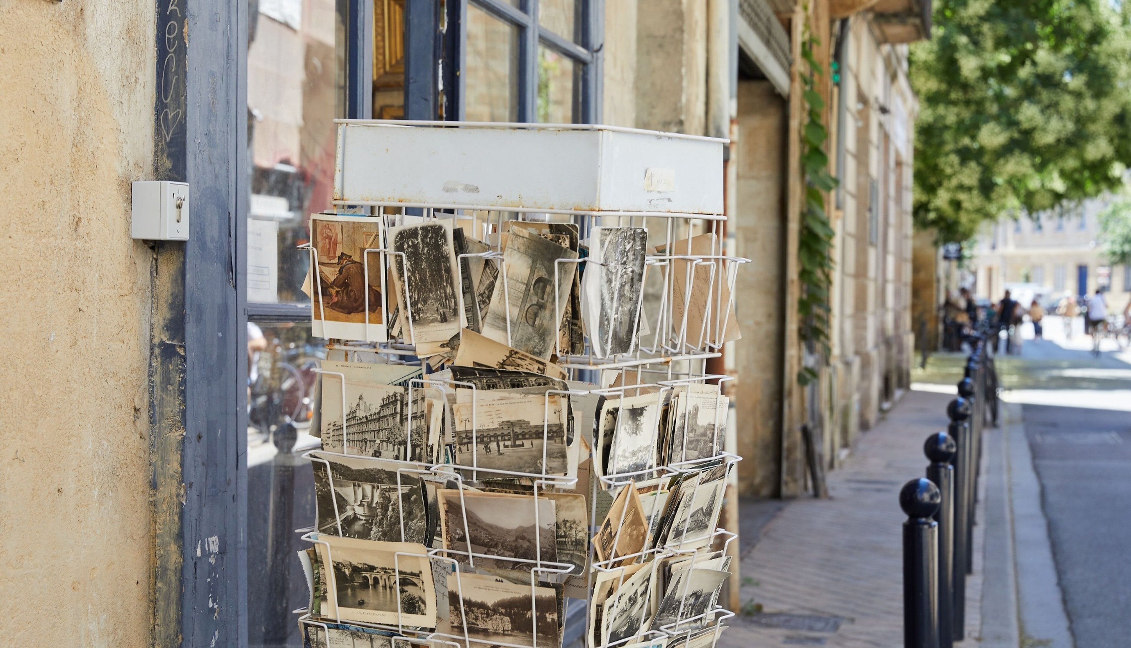 Une pile de cartes postales sur un présentoir métallique devant un bâtiment.