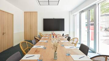 Un salón de conferencias con una larga mesa, sillas, una pantalla de proyector y un amplio ventanal.