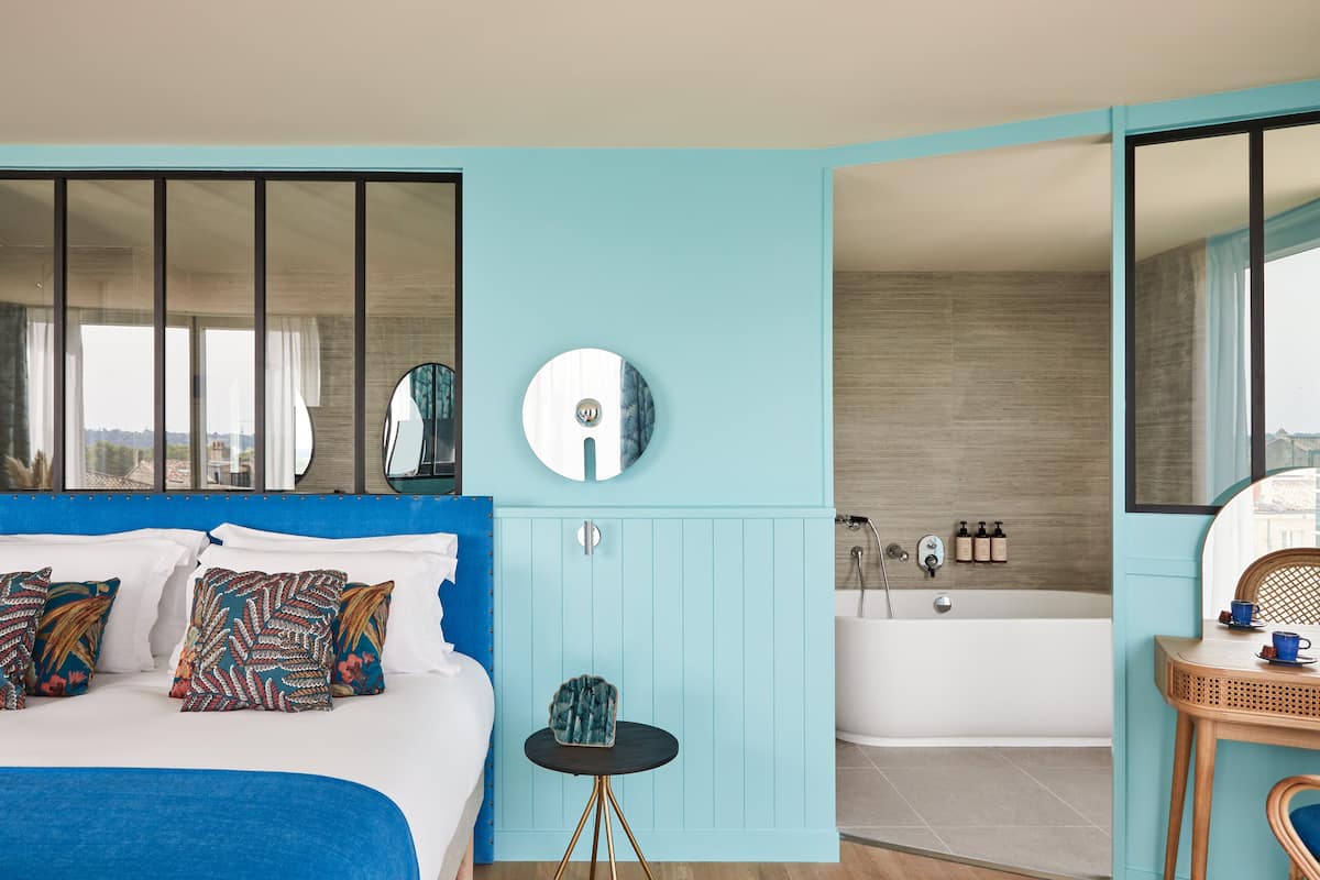 Ein modernes Schlafzimmer mit einem großen Bett, einem runden Spiegel, einem kleinen Tisch und einem Badezimmer mit Badewanne und Dusche.